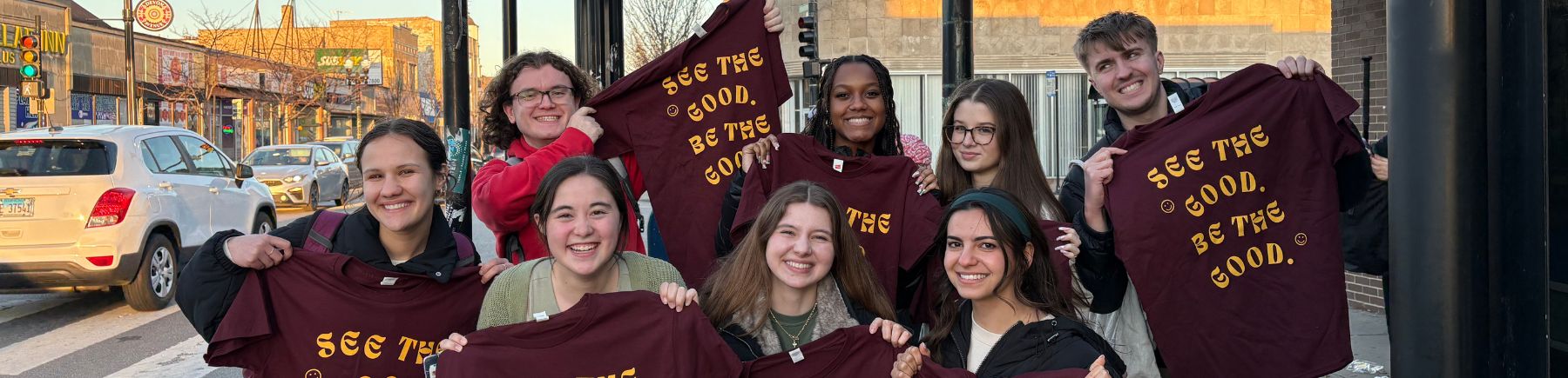 A group of volunteers smiling and holding maroon t-shirts.